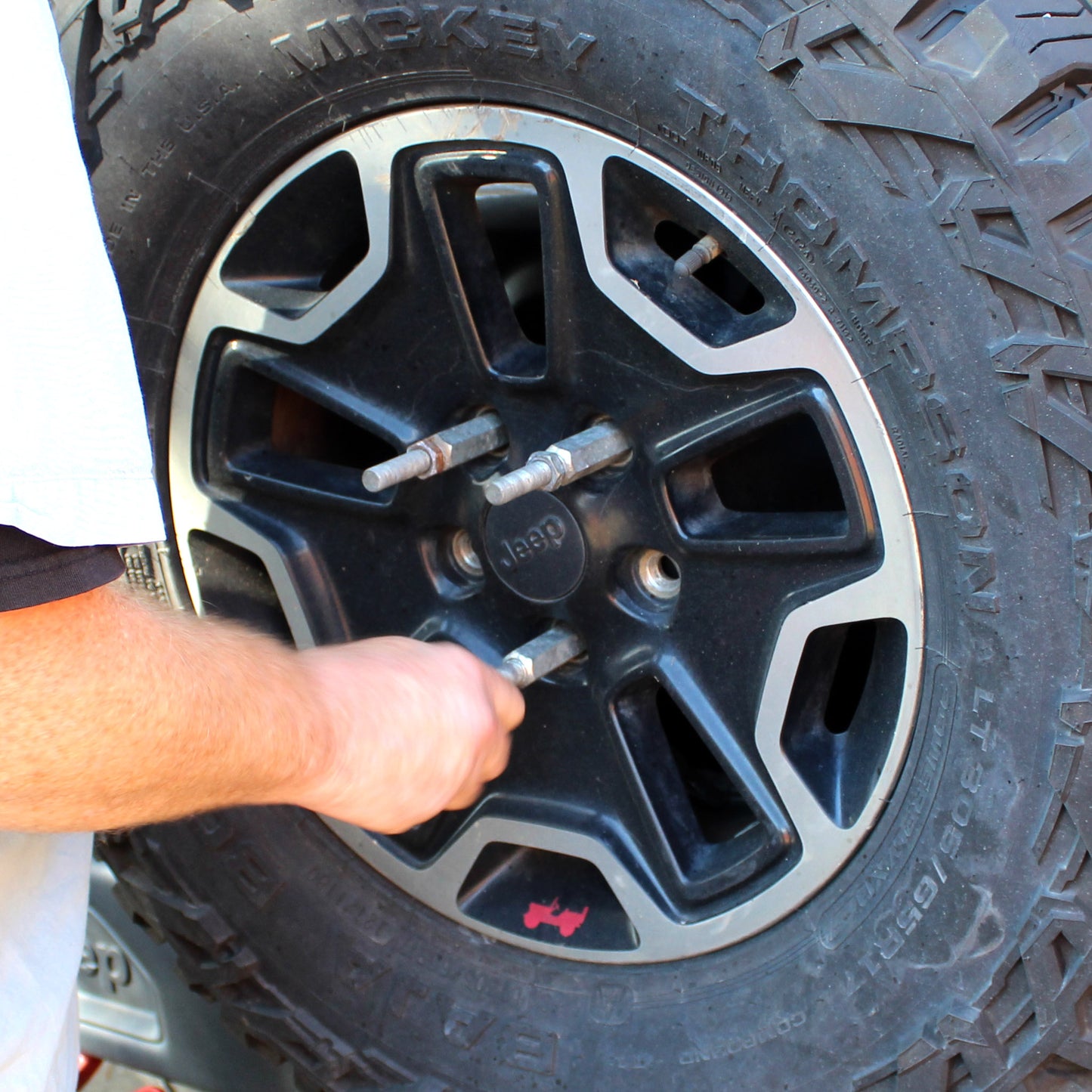 Person changing mounting a cargo carrier on a Jeep vehicle with a close-up of the wheel and hand.