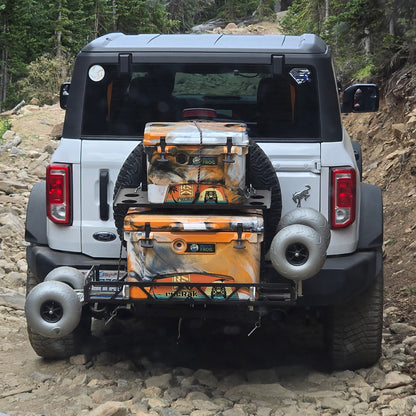 White Ford Bronco with camouflage coolers on a rocky trail